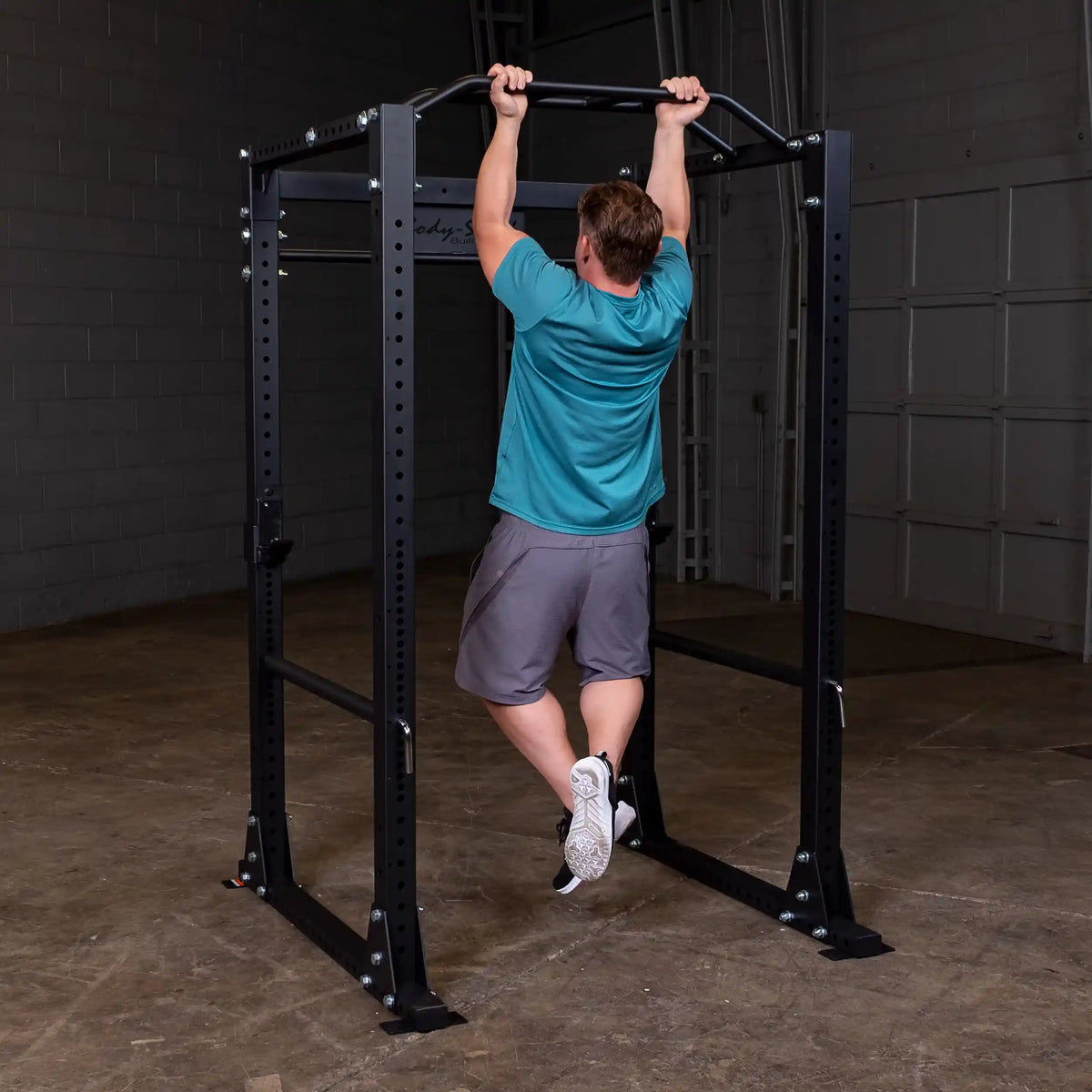 Man doing pull-up on black power rack in gym.