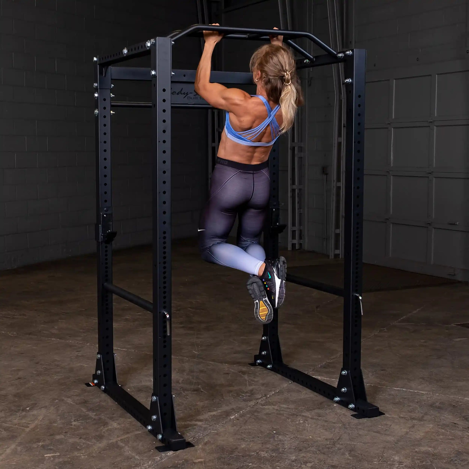 Woman doing pull-up on black power rack in gym.