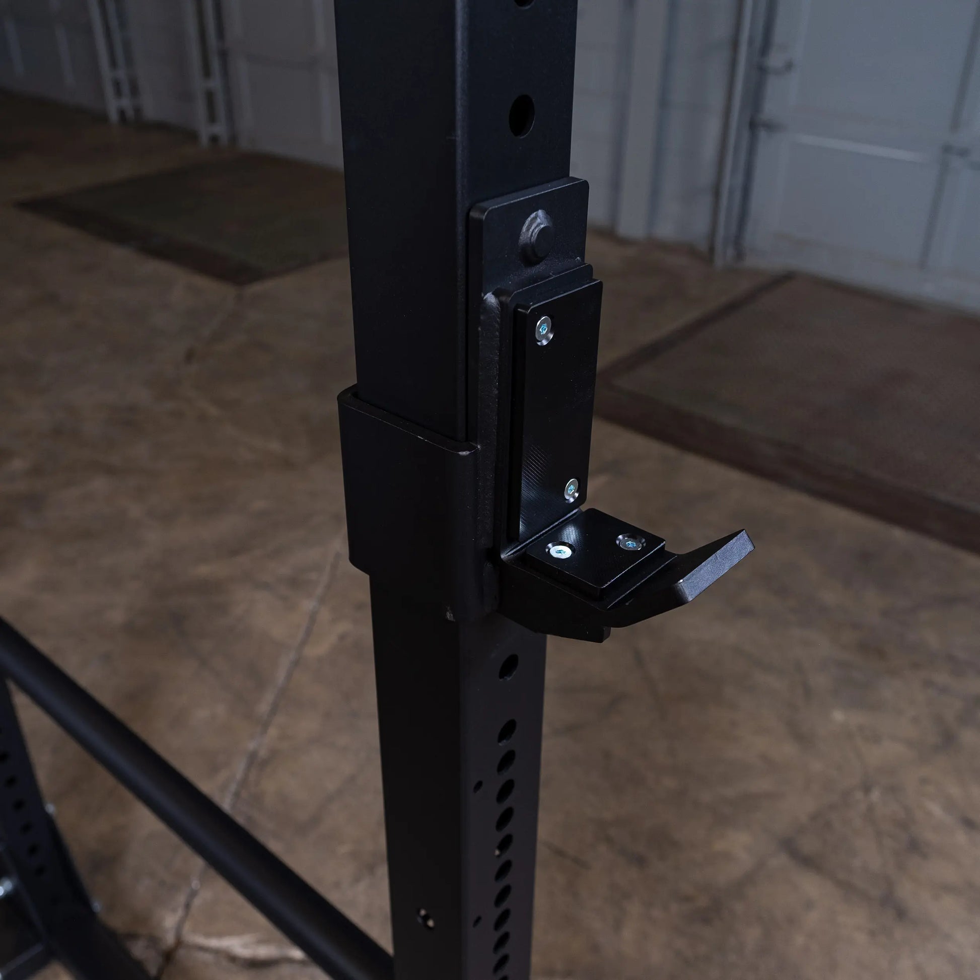 Black steel squat rack with adjustable J-hook in a garage gym setting.