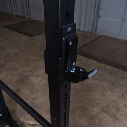 Black steel squat rack with adjustable J-hook in a garage gym setting.