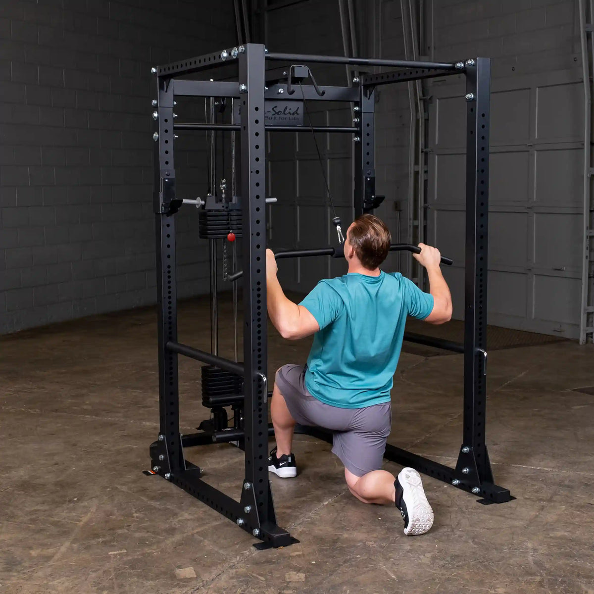 Man using a Body-Solid power rack for lat pulldowns in a gym.