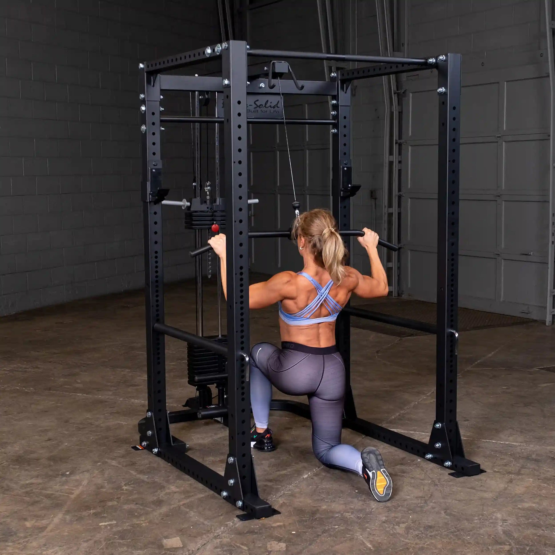 Woman using Body-Solid power rack for strength training in gym.