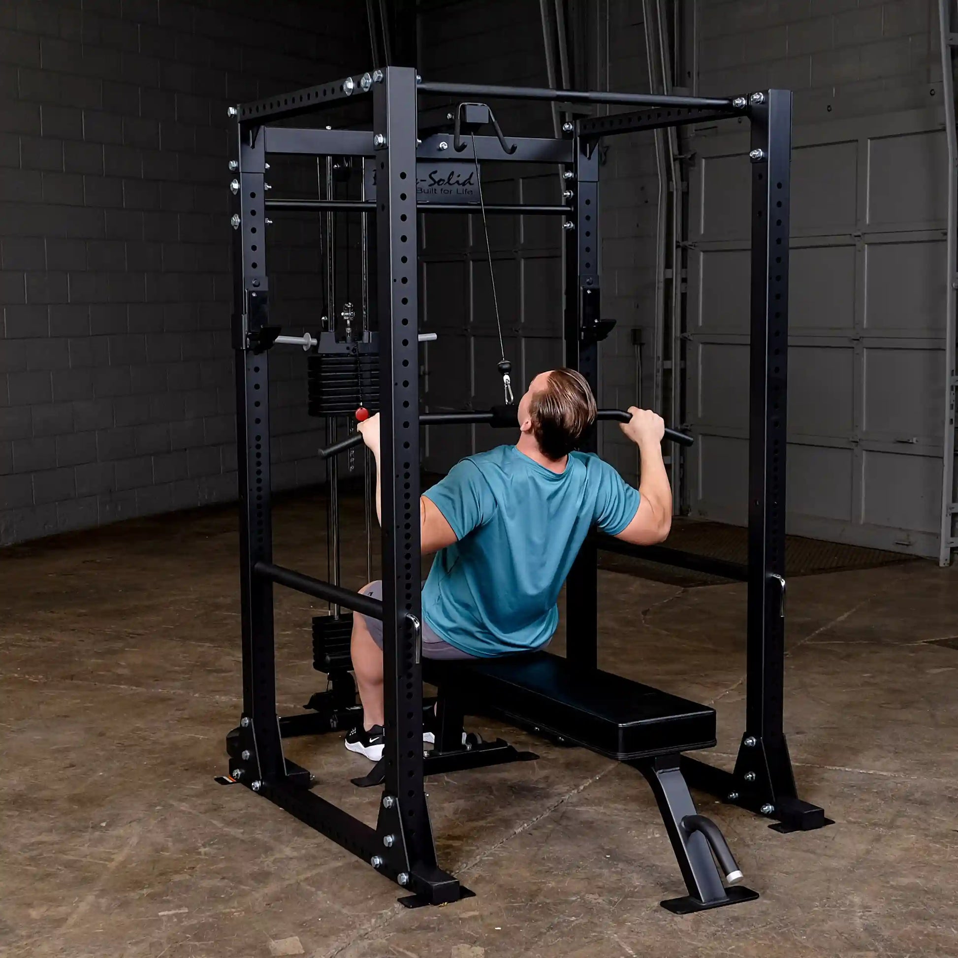 Man using Body-Solid power rack in gym for lat pulldown exercise.