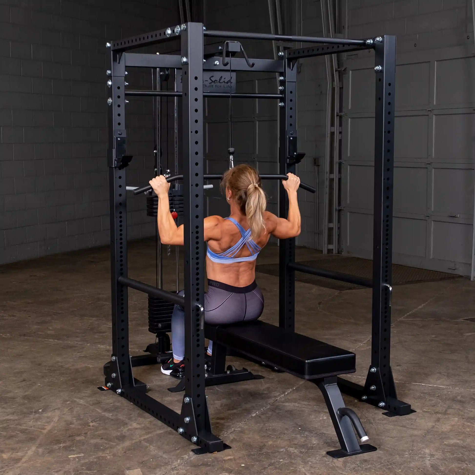 Woman using black power rack for lat pulldowns in a gym.