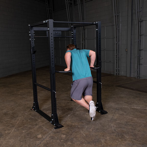 Man doing dips on black power rack in gym.