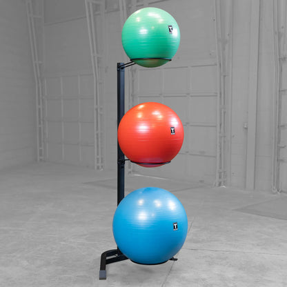 Stacked exercise balls on a black vertical rack, featuring green, red, and blue colors, in a spacious room.