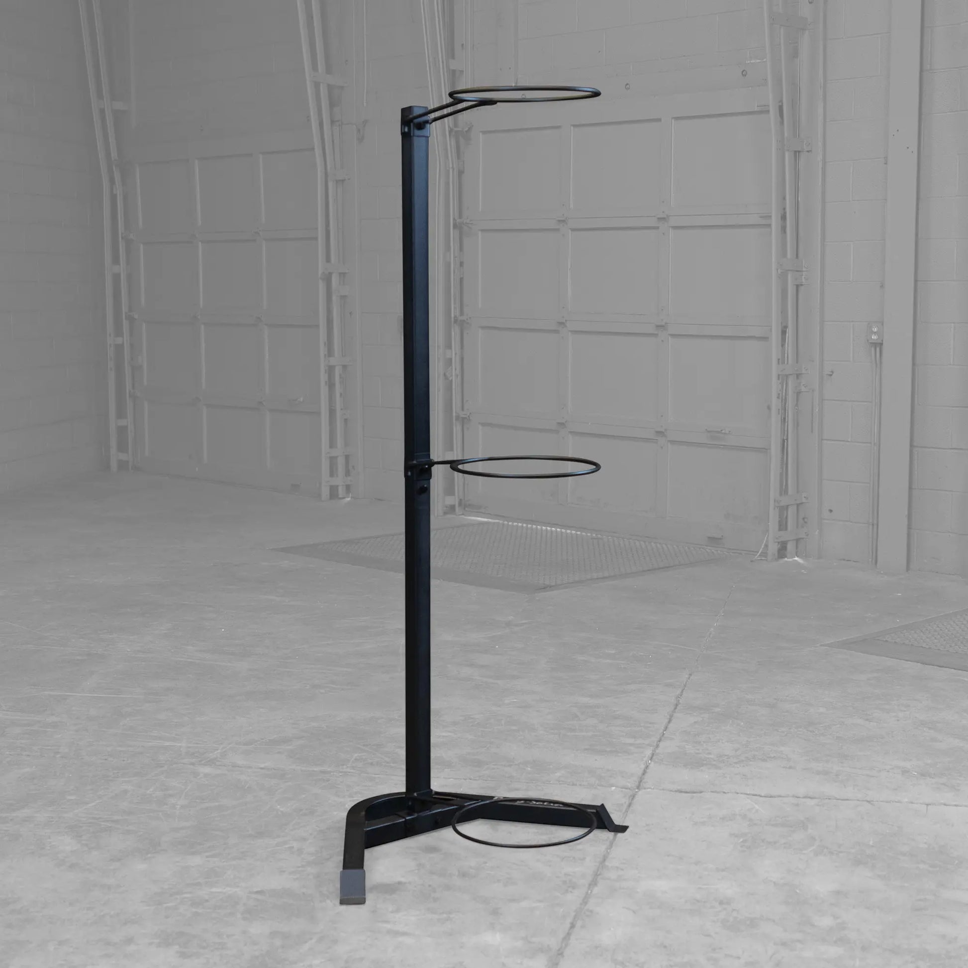 Black industrial trash bag holder with three rings in a warehouse setting.