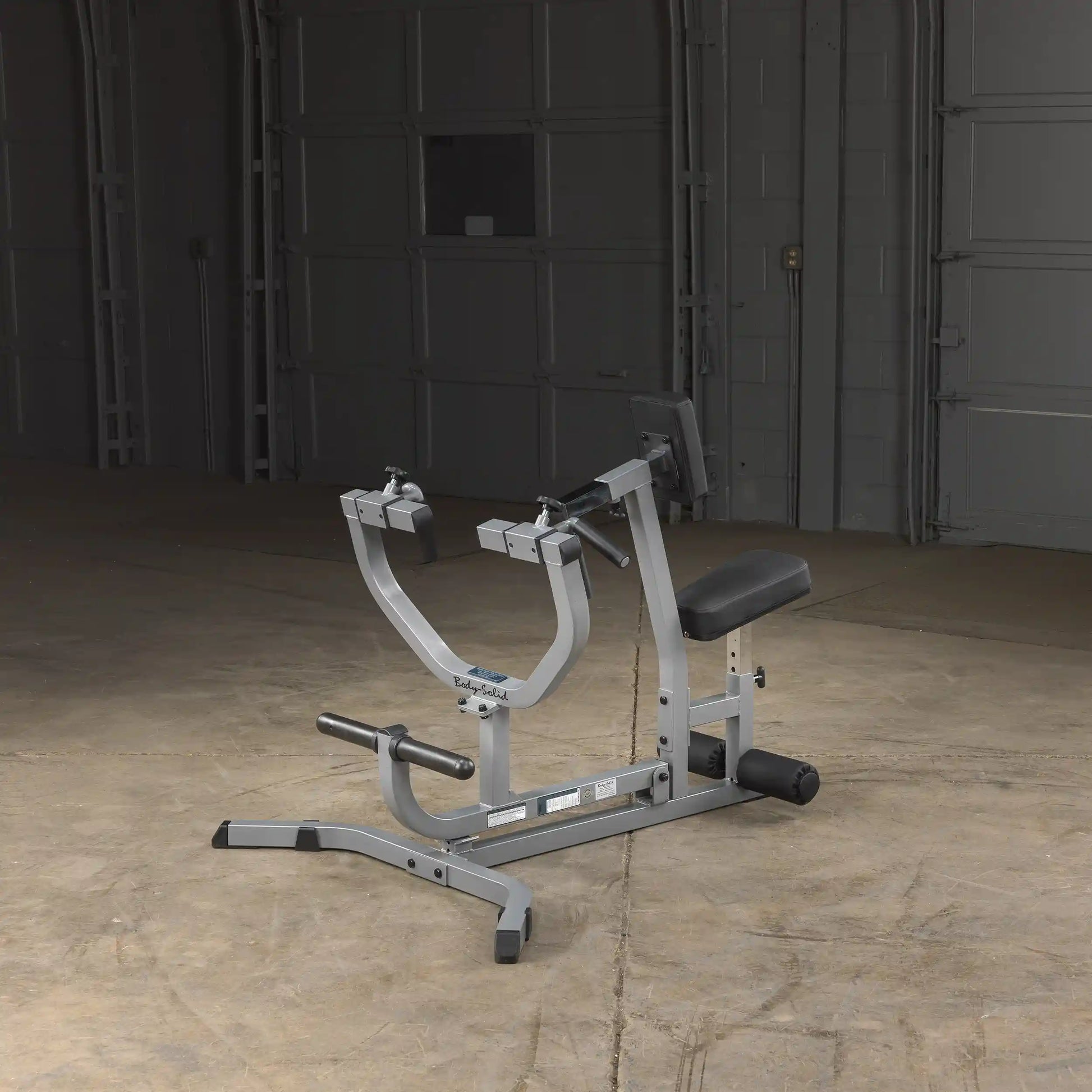 Body-Solid commercial bicep curl machine with adjustable seat in a garage gym setting.