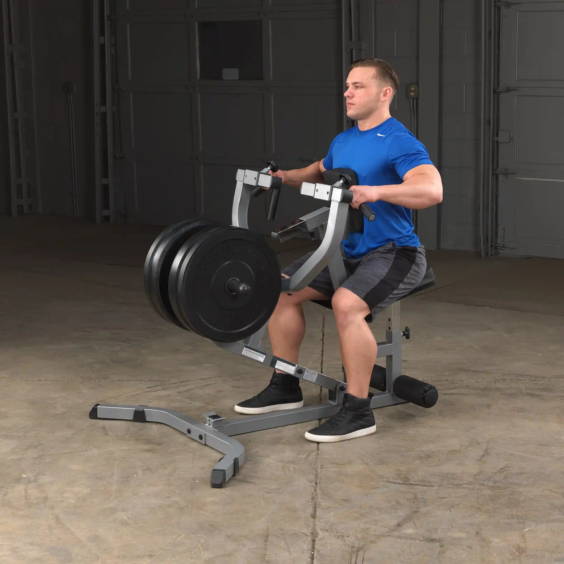 Man using a seated row machine with weights in a gym, wearing a blue shirt.
