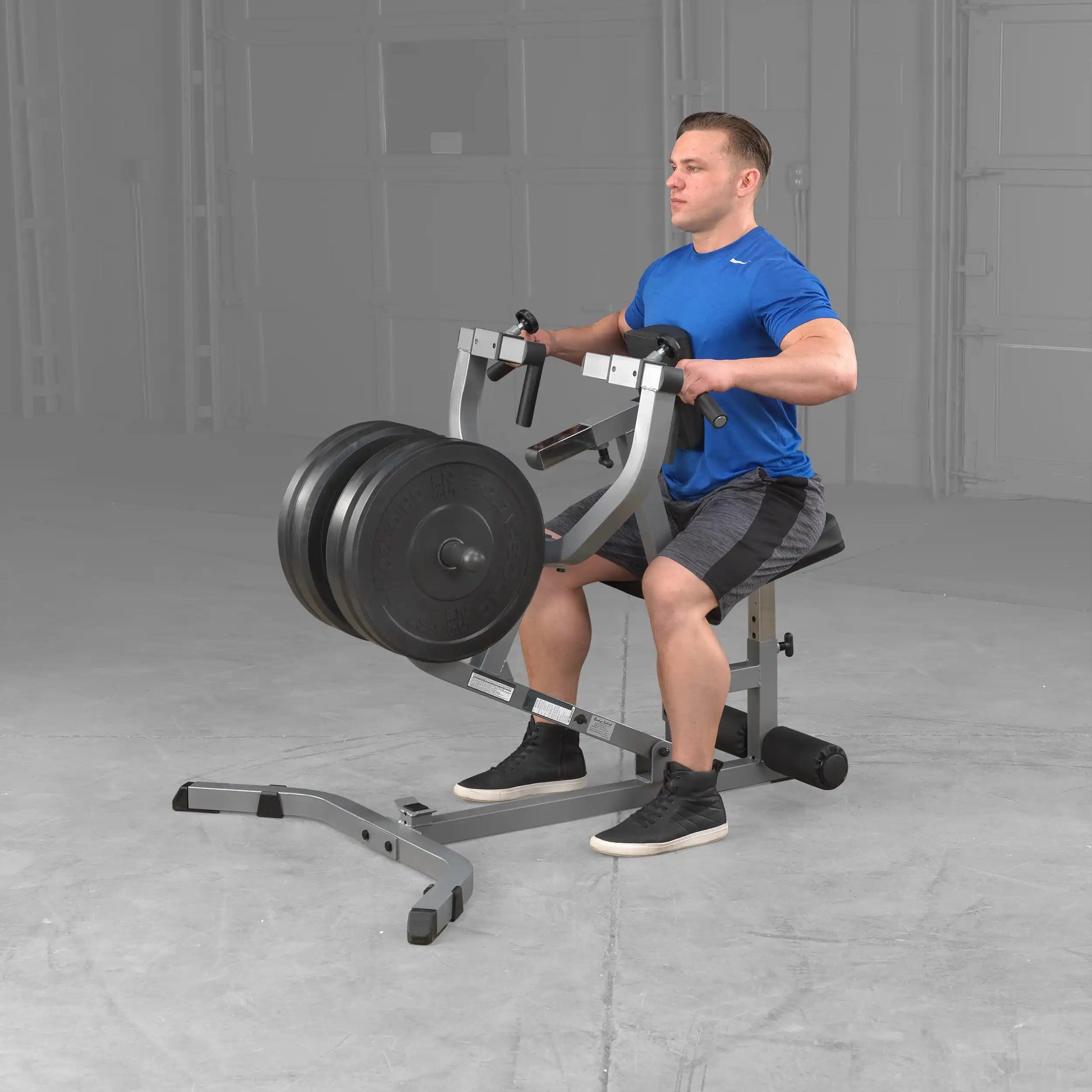 Man using a seated row machine with weights in a home gym, wearing a blue shirt.