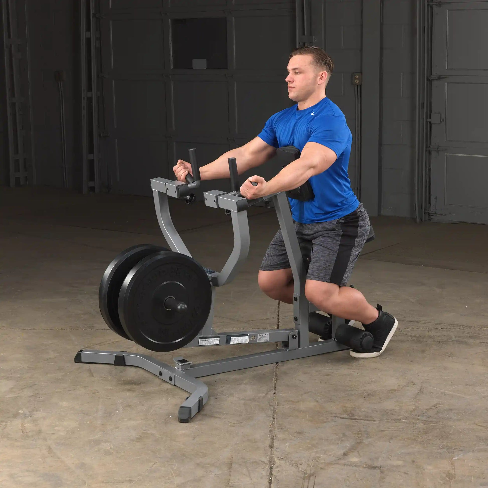 Man using a seated calf raise machine in a gym, wearing a blue shirt and gray shorts.