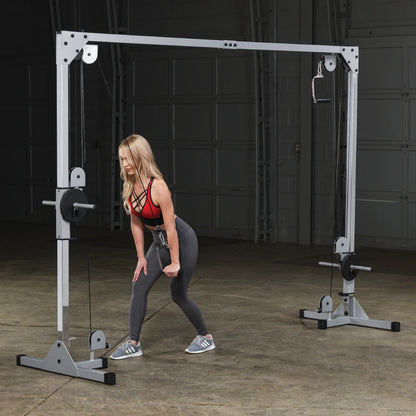 A woman in a red sports top and gray leggings performs a cable exercise using a fitness machine in a gym setting.