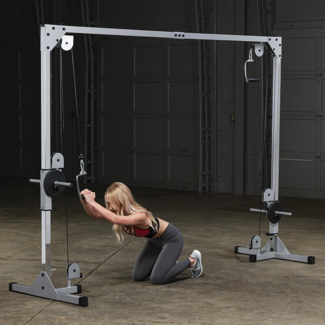 A person kneeling on the floor in a gym, using a cable machine for strength training exercises.