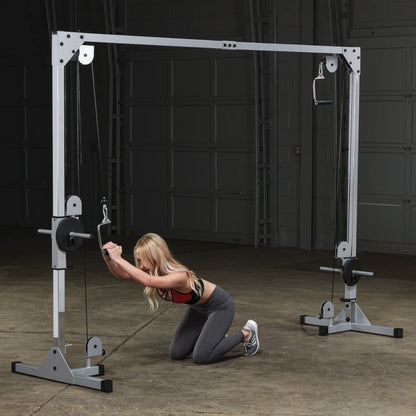 A person kneeling on the floor in a gym, using a cable machine for strength training exercises.