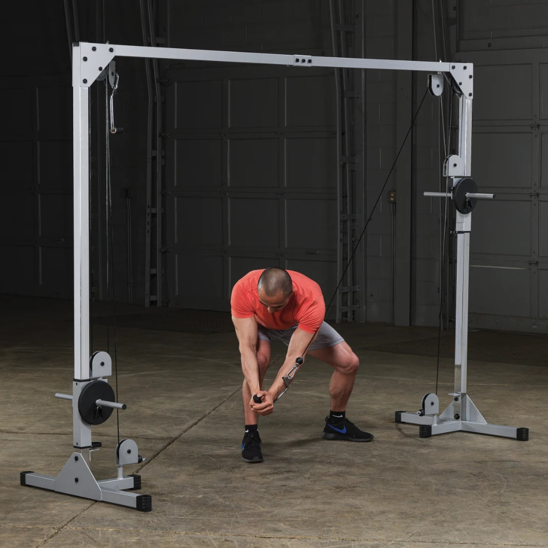 A man in an orange shirt and gray shorts performs a cable exercise using a cable machine in a gym setting, focusing on strength training.