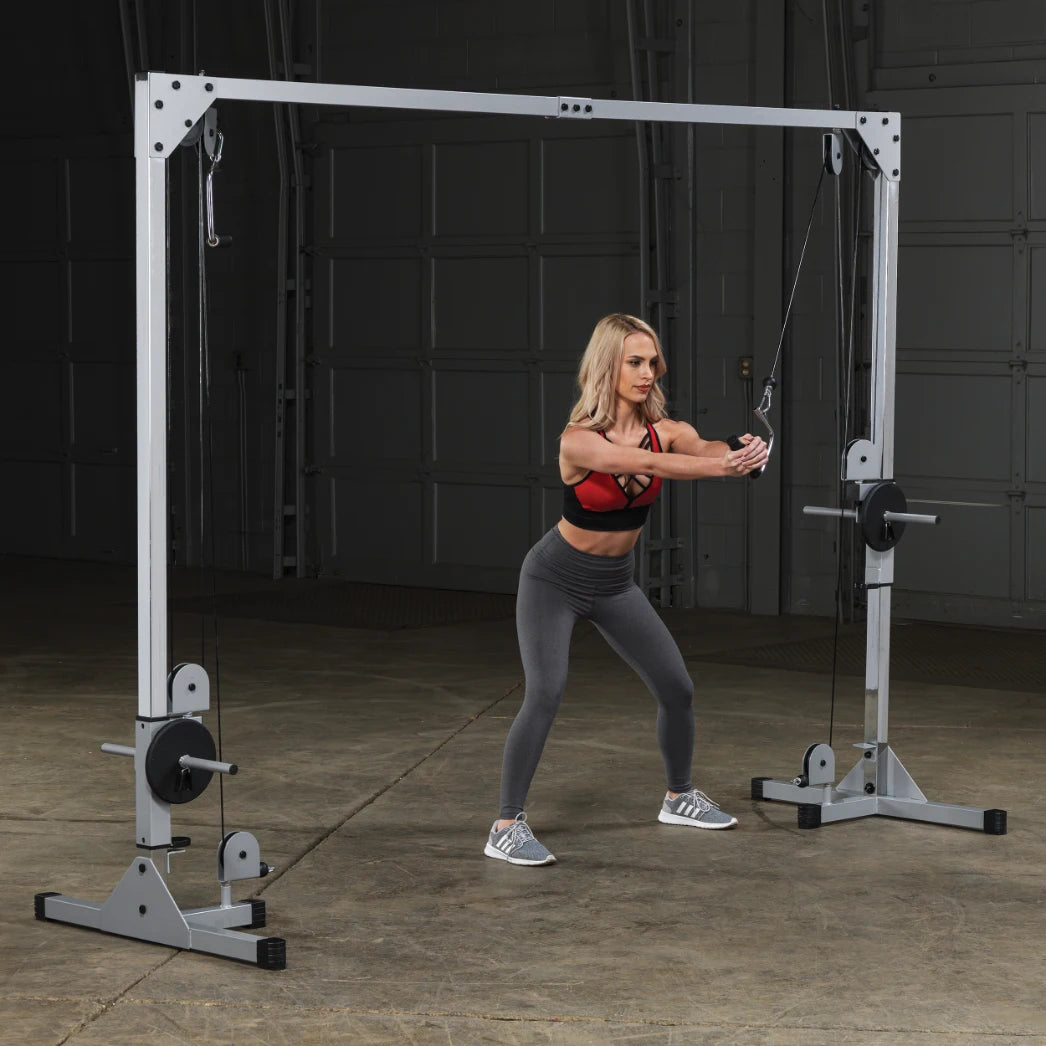 A woman performing a cable exercise in a gym setting, using a cable machine with a focused expression, wearing a red sports bra and gray leggings.