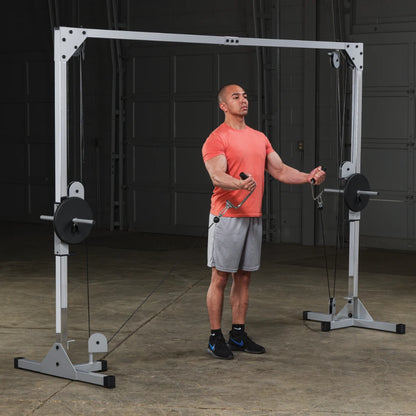 A man in an orange shirt and gray shorts performs a cable exercise using a cable machine in a gym setting, focusing on strength training.