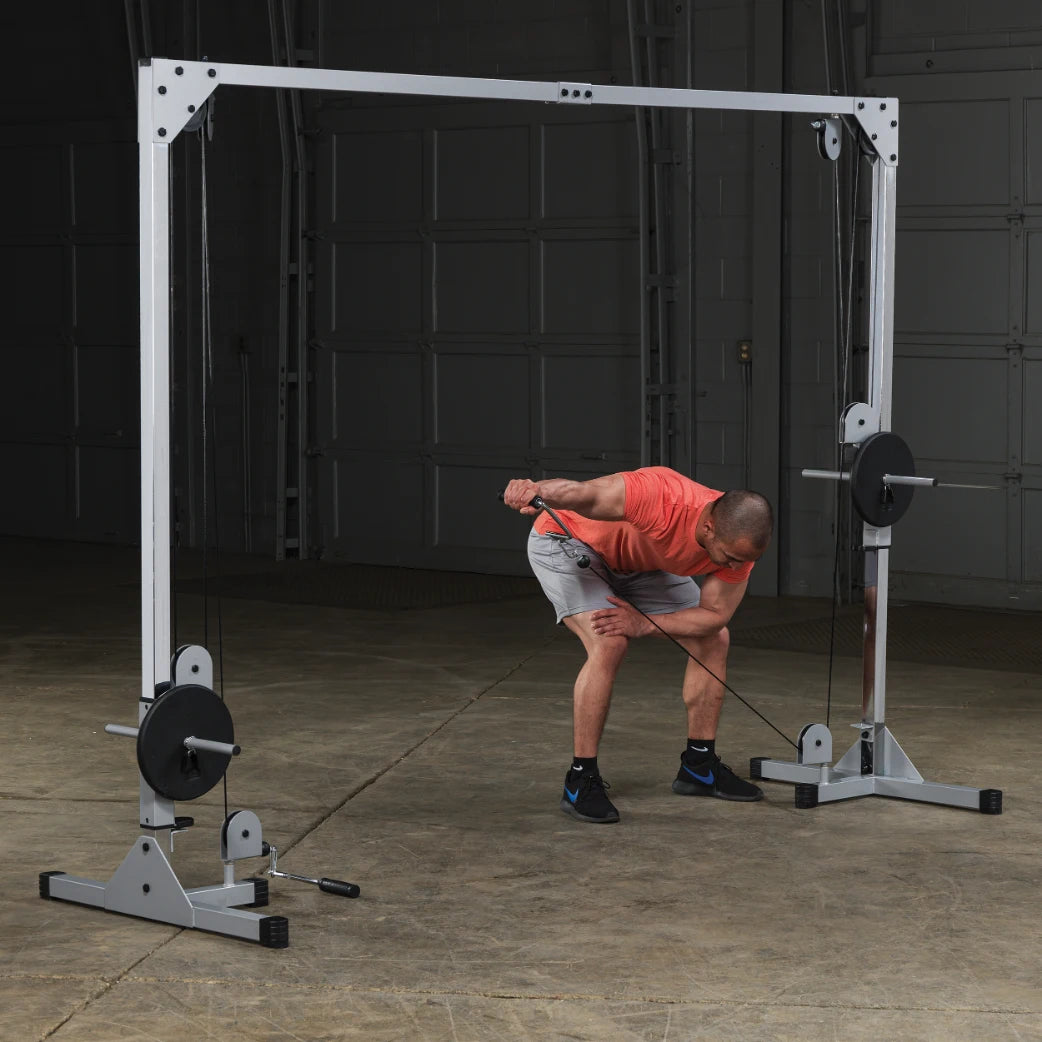 A person in a red shirt and gray shorts is performing a cable exercise using a dual pulley machine in a gym setting. The individual is bent slightly forward, gripping the cable handle with one hand while adjusting their stance.