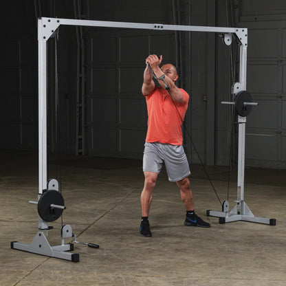 A man in an orange shirt and gray shorts performing a cable exercise using a gym machine, demonstrating strength training techniques in a spacious indoor setting.