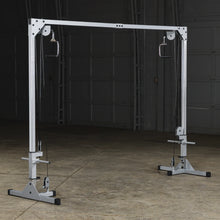 A functional cable machine for strength training, featuring adjustable pulleys and grips, set in an empty gym space with a concrete floor.