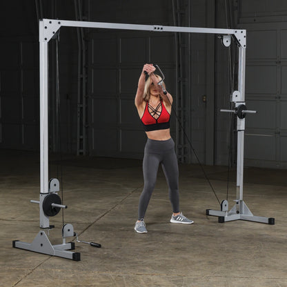 A woman in a red sports bra and gray leggings performs a cable exercise using a cable machine in a gym setting.