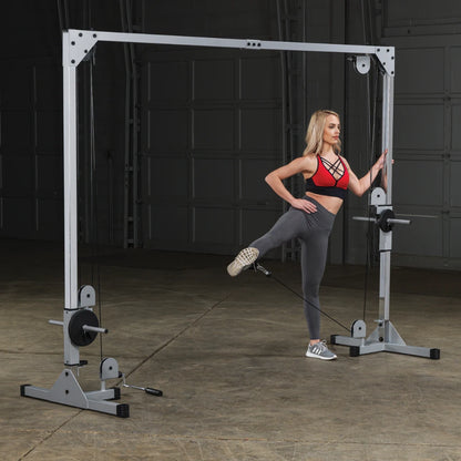 A woman in a red sports bra and gray leggings performs a leg exercise using a cable machine in a gym setting.