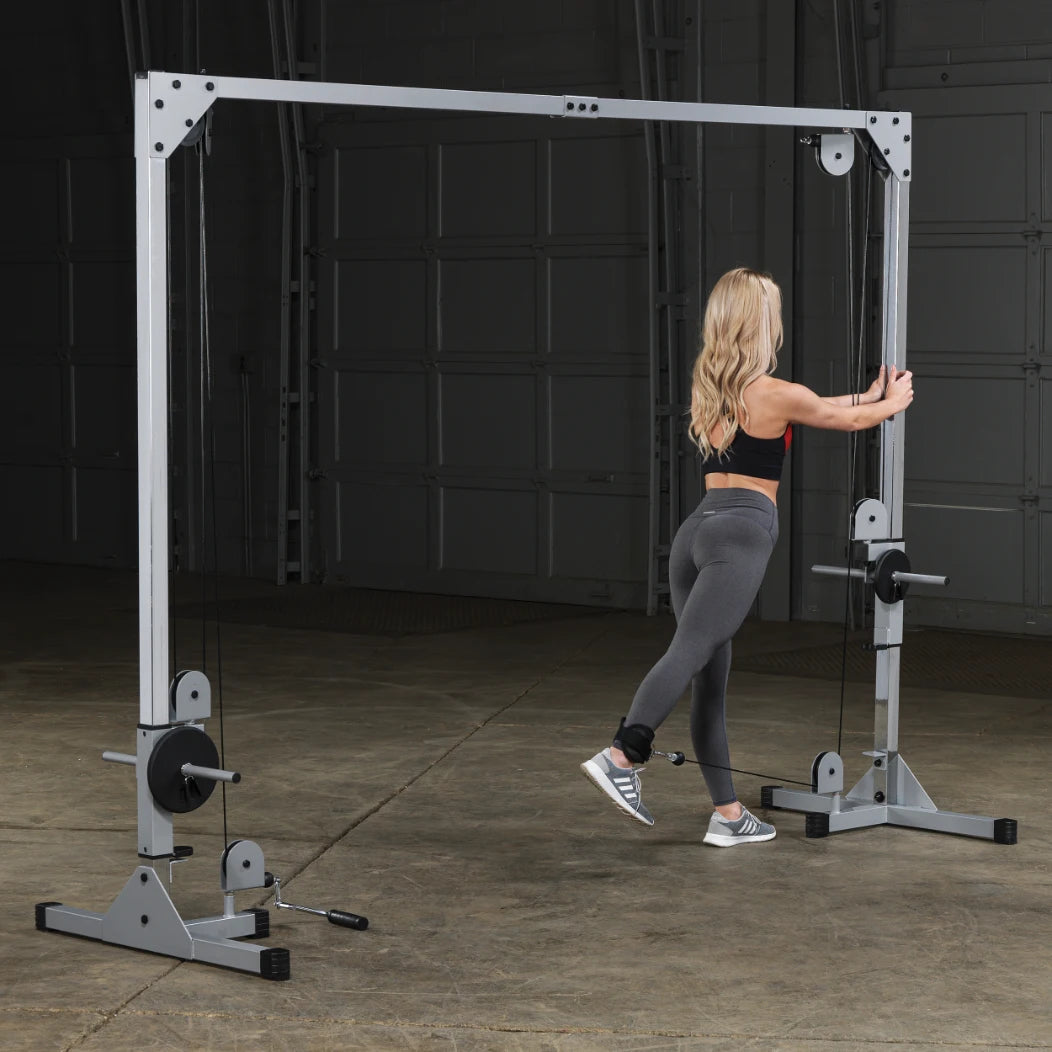 A woman in athletic wear performs an exercise on a cable machine in a gym setting, focusing on her leg workout.