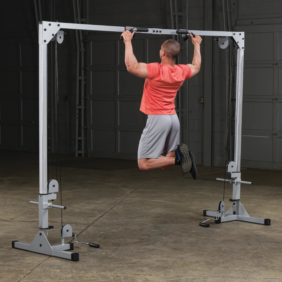 A person performing a pull-up on a fitness machine in a gym setting, wearing a red shirt and gray shorts, demonstrating strength training.