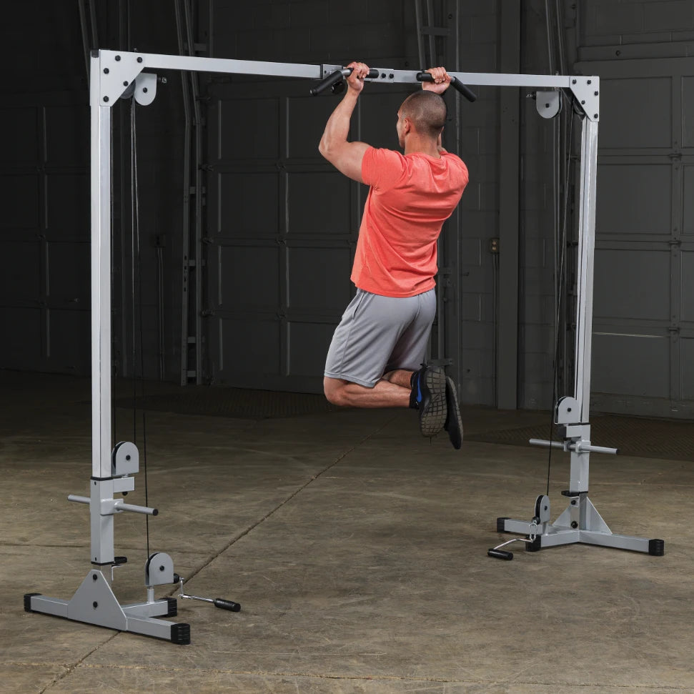 A man in a red shirt and gray shorts performing a pull-up on a fitness machine in a gym setting.