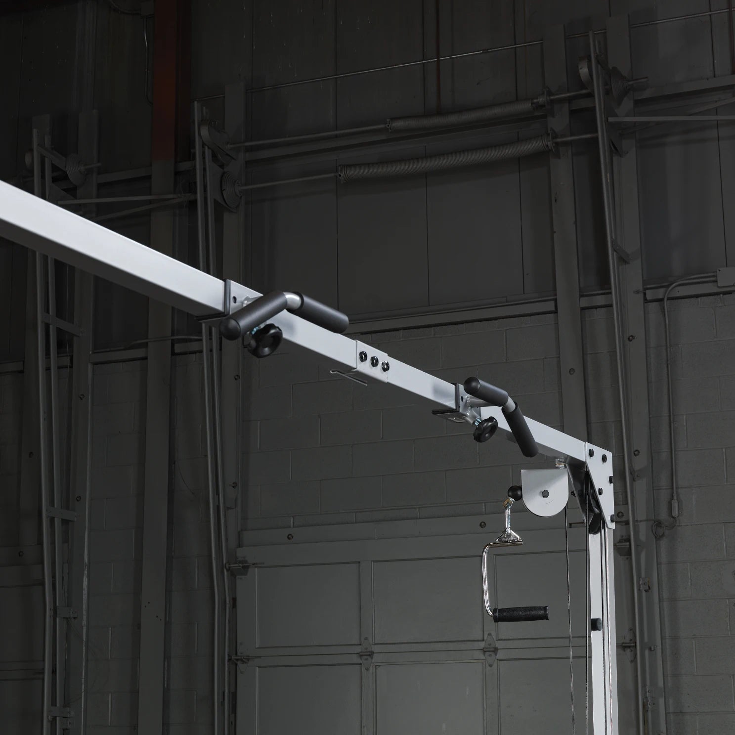 Close-up of a gym cable machine showing the pulley system and handle, set against a dark industrial background.