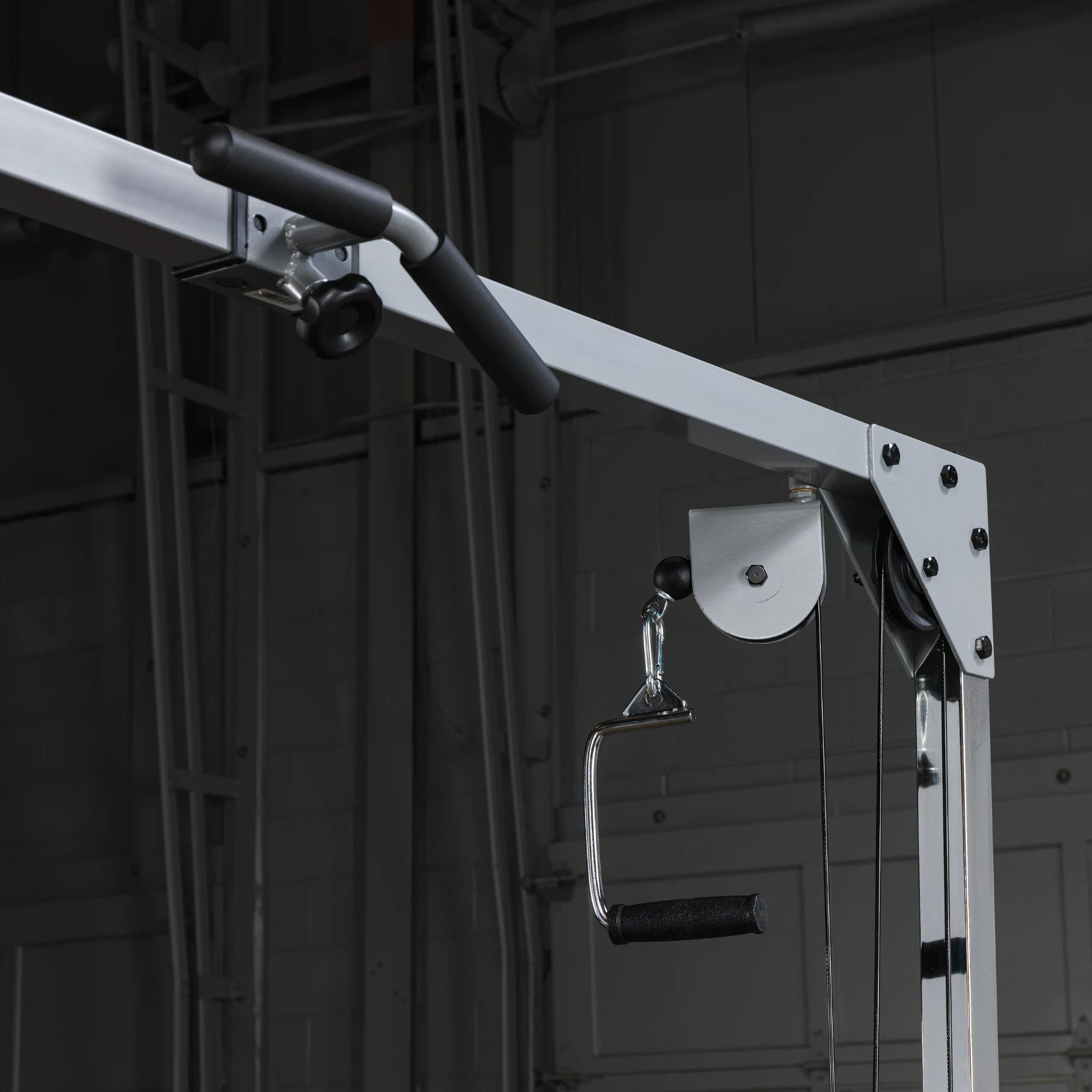 Close-up of a cable machine attachment, featuring a metal handle with a textured grip and a pulley system, set against a dark gym background.