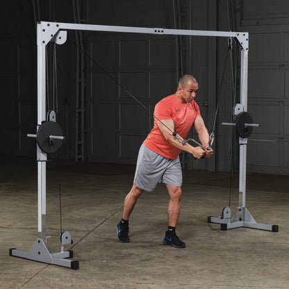 A man in a red shirt and gray shorts performs a cable exercise using a cable machine in a gym setting.