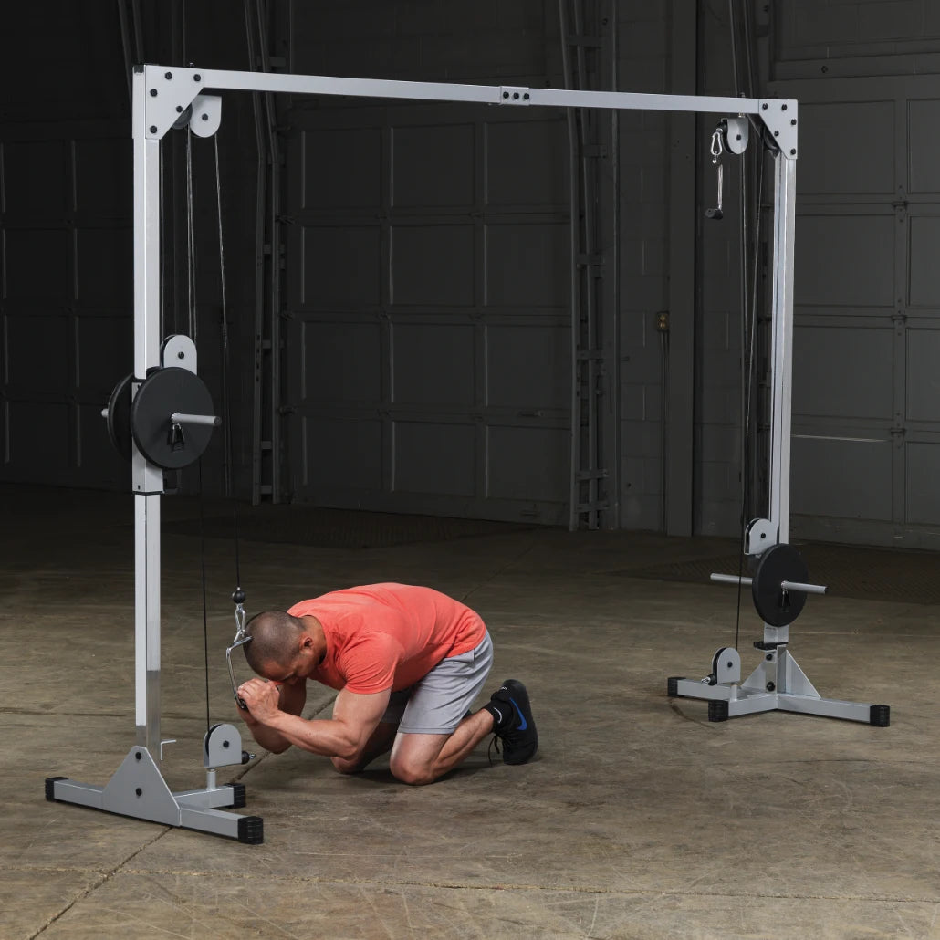 A man in a red shirt and gray shorts performing a workout on a cable machine, kneeling and using the equipment in a gym setting.