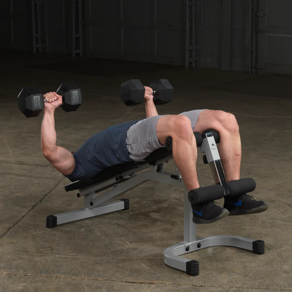 A person performing a dumbbell exercise while lying on a bench, holding weights above their chest, with feet secured in a leg brace.