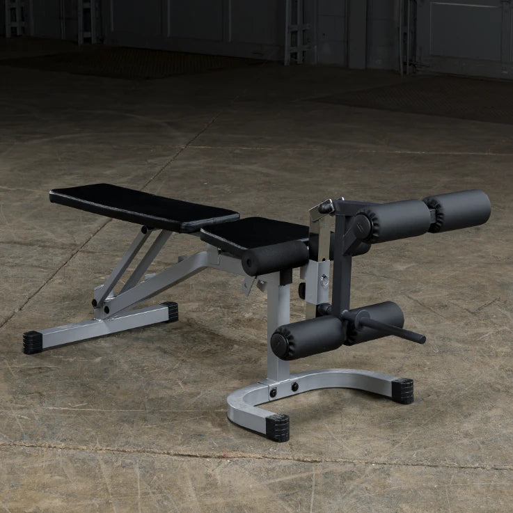 A weight bench with adjustable features, including padded seating and leg rollers, set against a concrete floor in a gym environment.