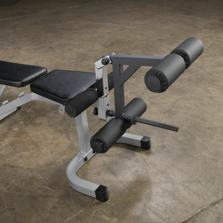A close-up view of a gym exercise machine designed for leg curls, featuring adjustable padded rollers and a sturdy metal frame, set against a textured floor.