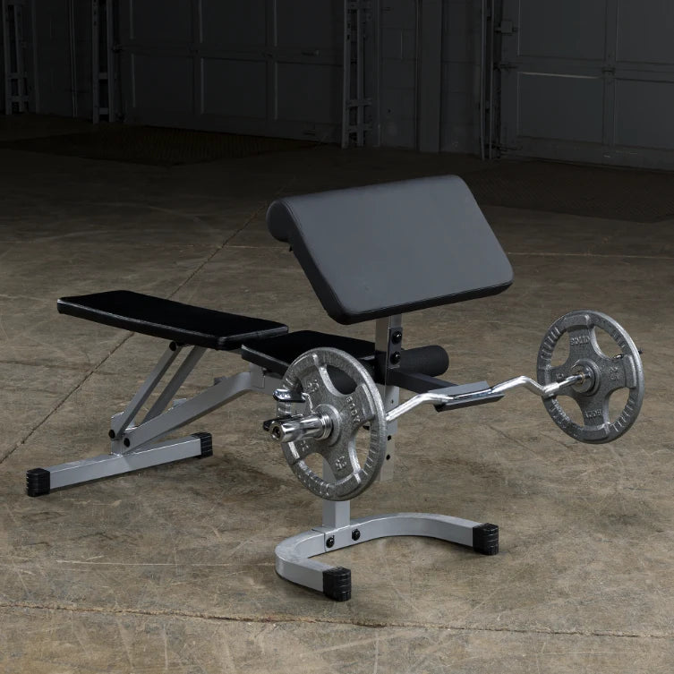 A silver and black adjustable weight bench with a barbell and weight plates, set on a concrete floor in a gym-like environment.