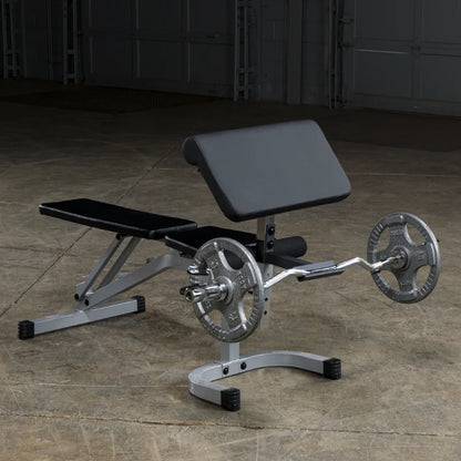 A silver and black adjustable weight bench with a barbell and weight plates, set on a concrete floor in a gym-like environment.