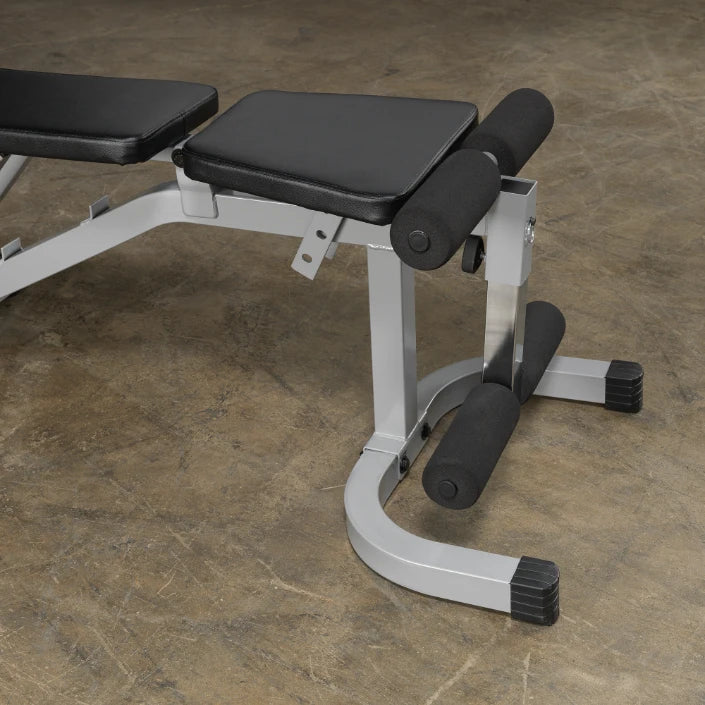 A close-up view of a black and silver adjustable weight bench, featuring padded seats and supports for leg exercises, set against a textured floor.