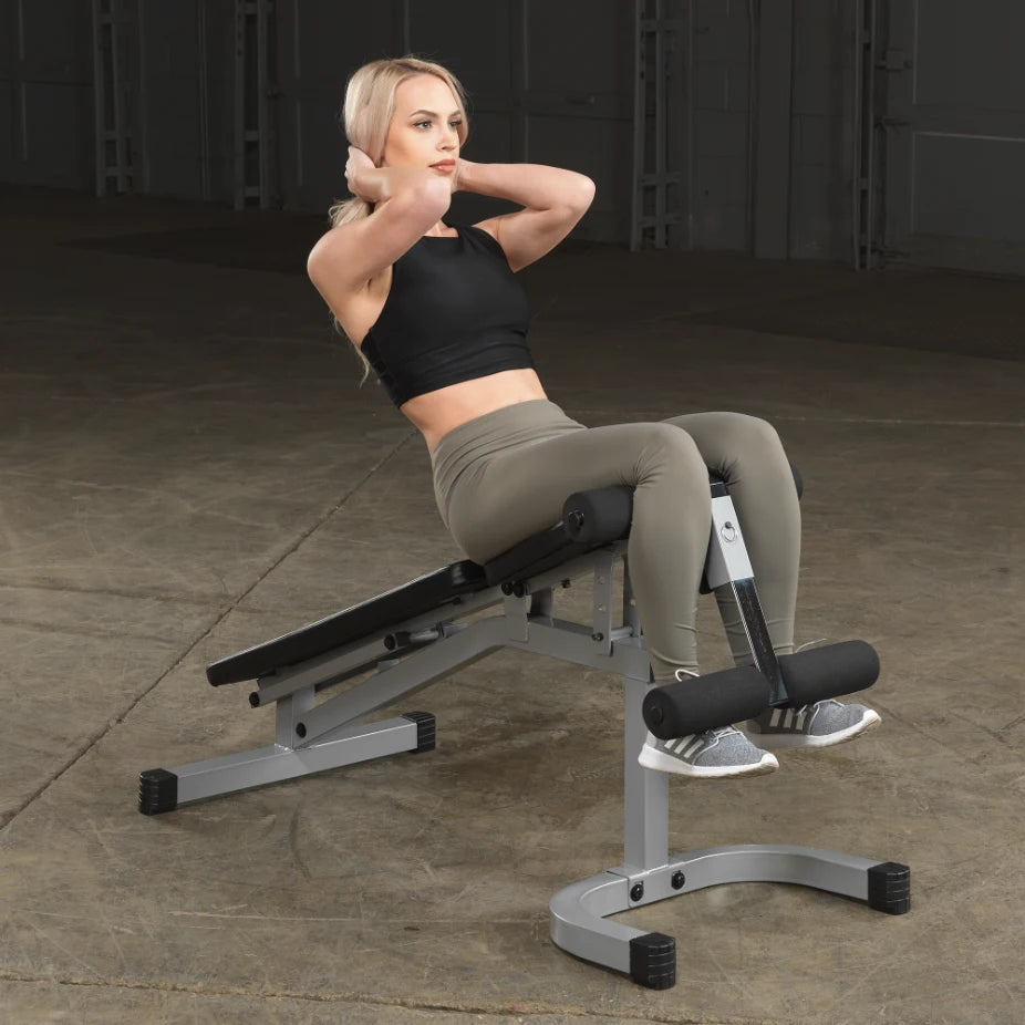 A woman performing abdominal exercises on a workout bench in a gym setting, wearing a black crop top and green leggings.