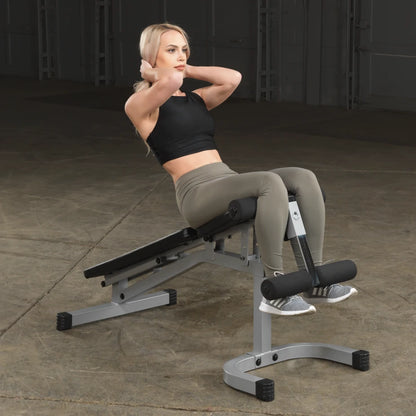 A woman performing abdominal exercises on a workout bench in a gym setting, wearing a black crop top and green leggings.
