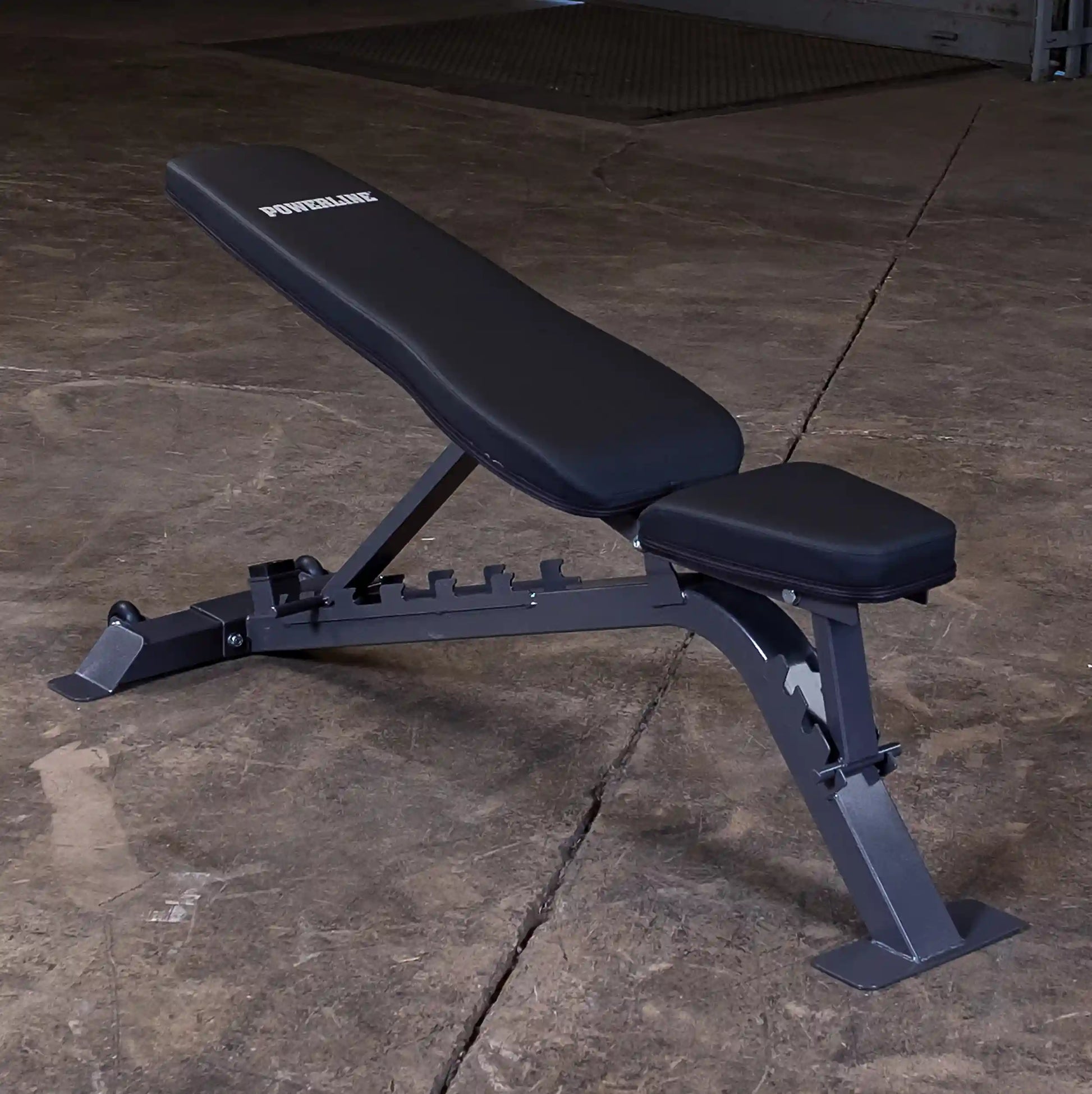 Adjustable weight bench with a black padded seat and backrest, set against a concrete floor. The bench is branded POWERLINE.