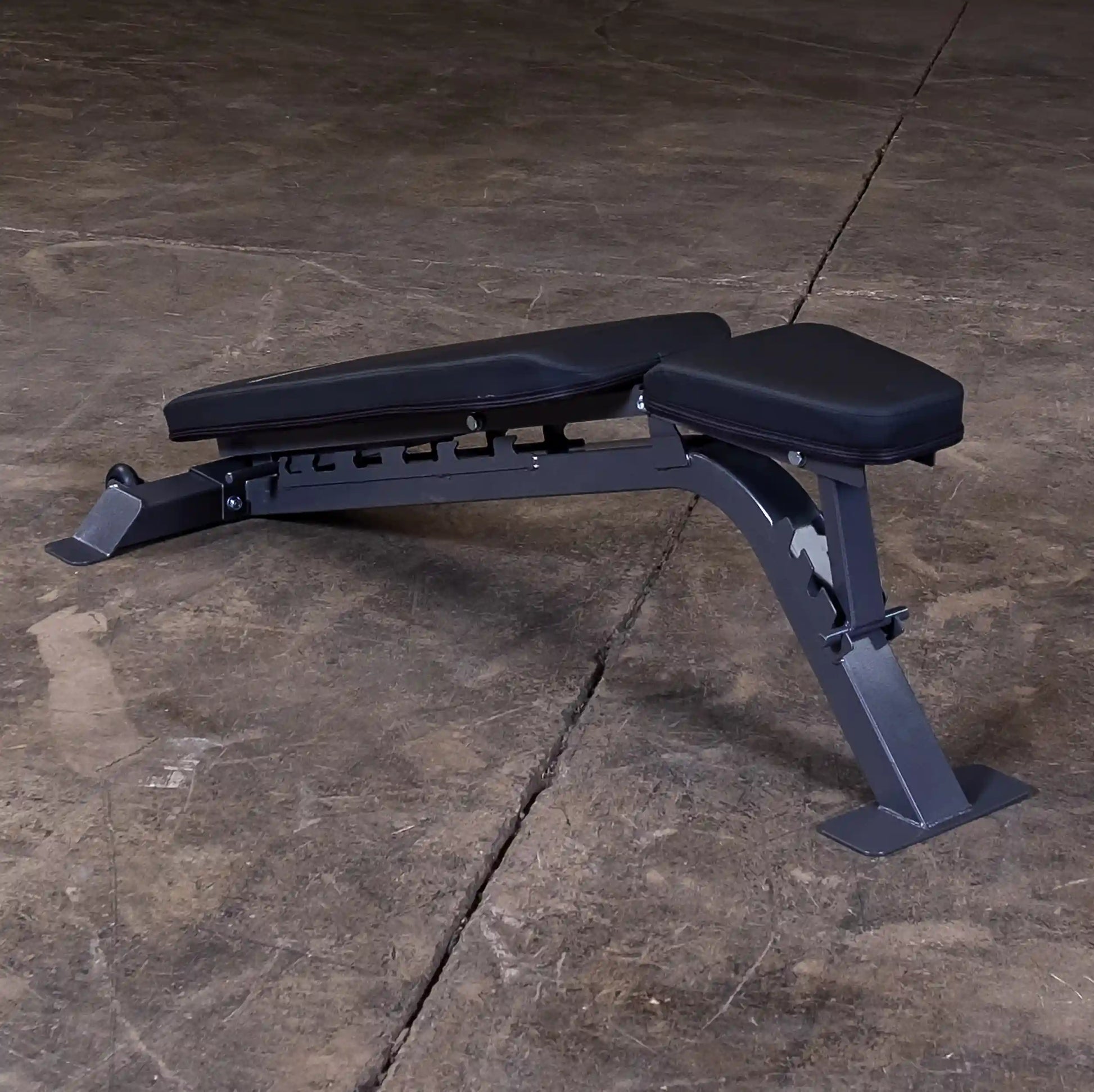 A black adjustable weight bench positioned on a concrete floor, showcasing its sturdy metal frame and padded seating for strength training exercises.