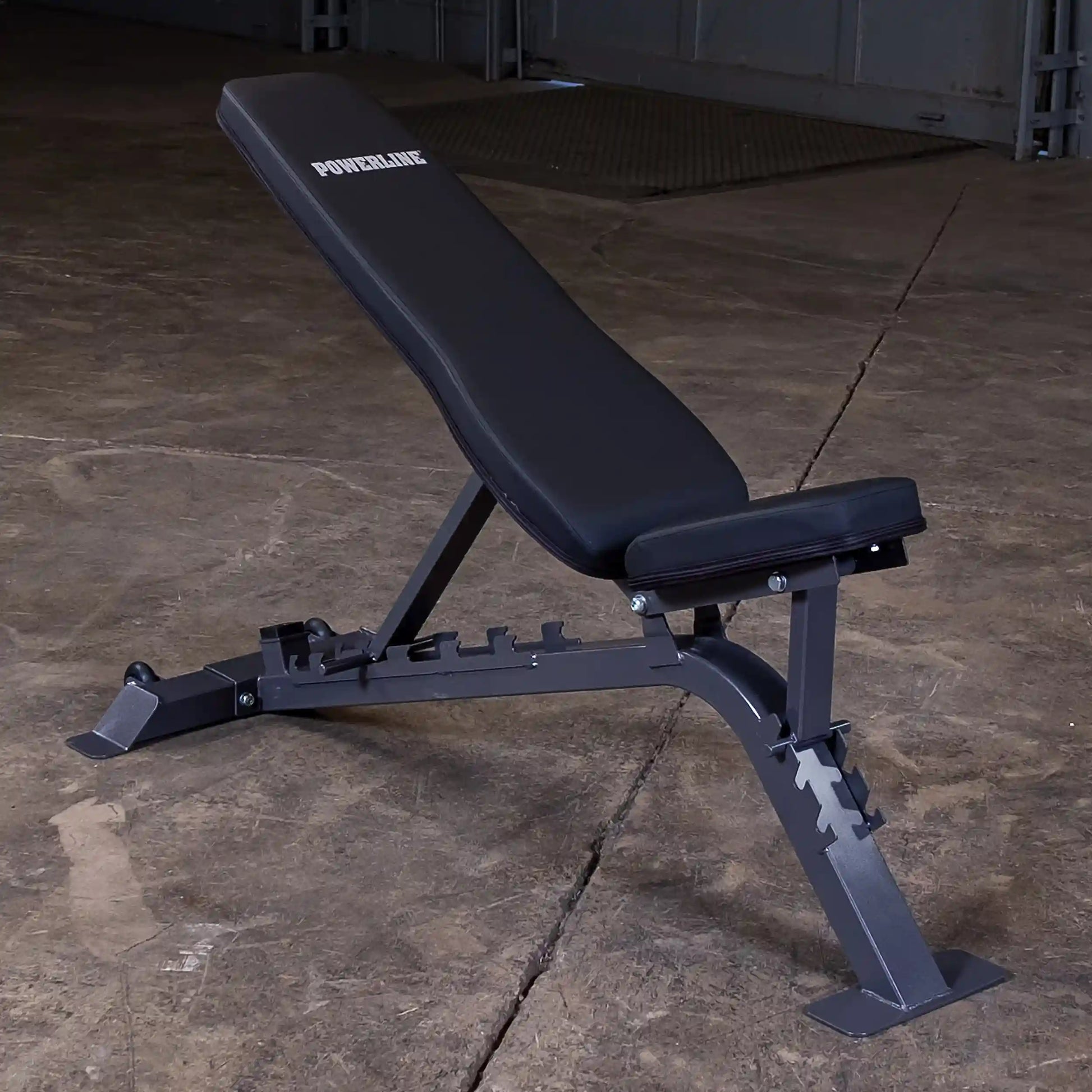 Adjustable weight bench with a black padded seat and backrest, featuring the brand name POWERLINE, set against a concrete floor.