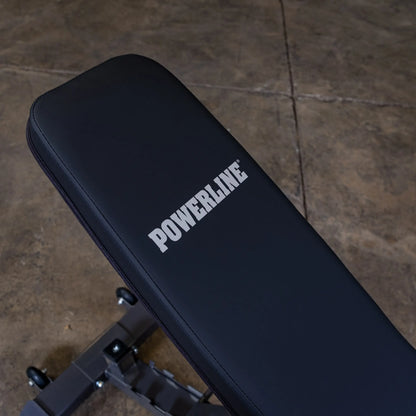 Close-up of a black workout bench with the word POWERLINE prominently displayed in white on the padded surface. The bench is positioned on a concrete floor.