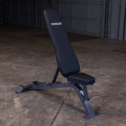 A black adjustable weight bench with the brand name POWERLINE displayed on the backrest, set against a concrete floor in a dimly lit garage.