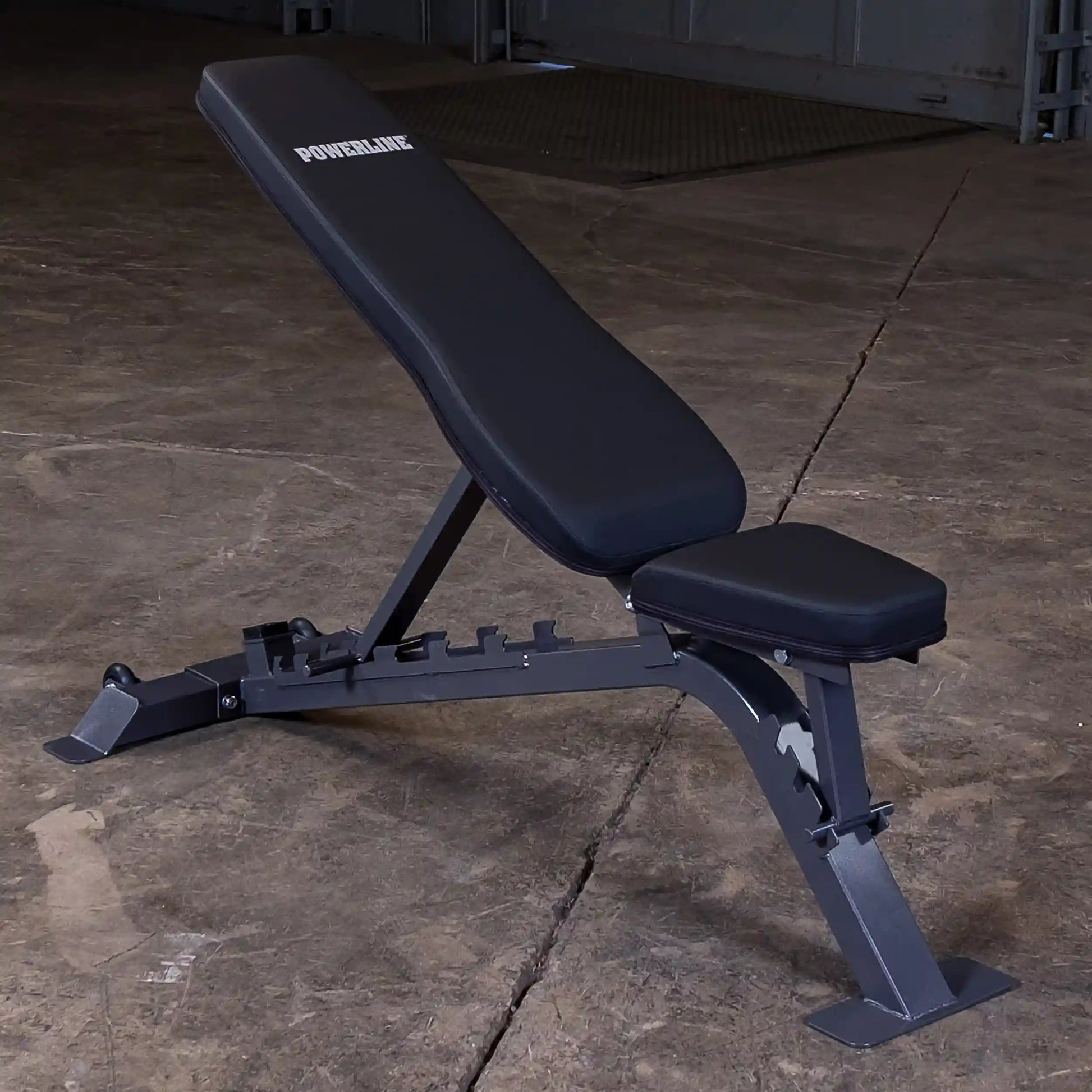 A black adjustable weight bench with the brand name POWERLINE displayed on the backrest, set against a concrete floor background.