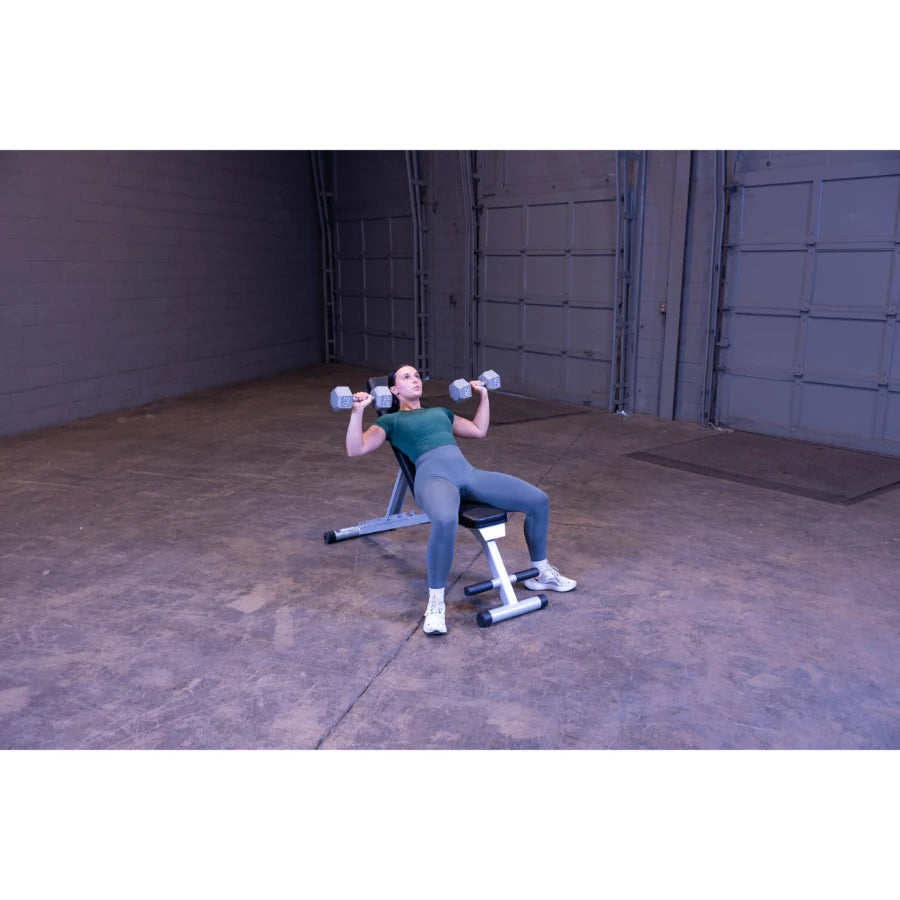 A person performing a chest press exercise on a bench, holding dumbbells in each hand, in a spacious indoor gym setting.