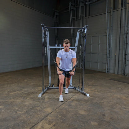 A young man in a white t-shirt and shorts performs a cable exercise using a fitness machine in a spacious gym setting.
