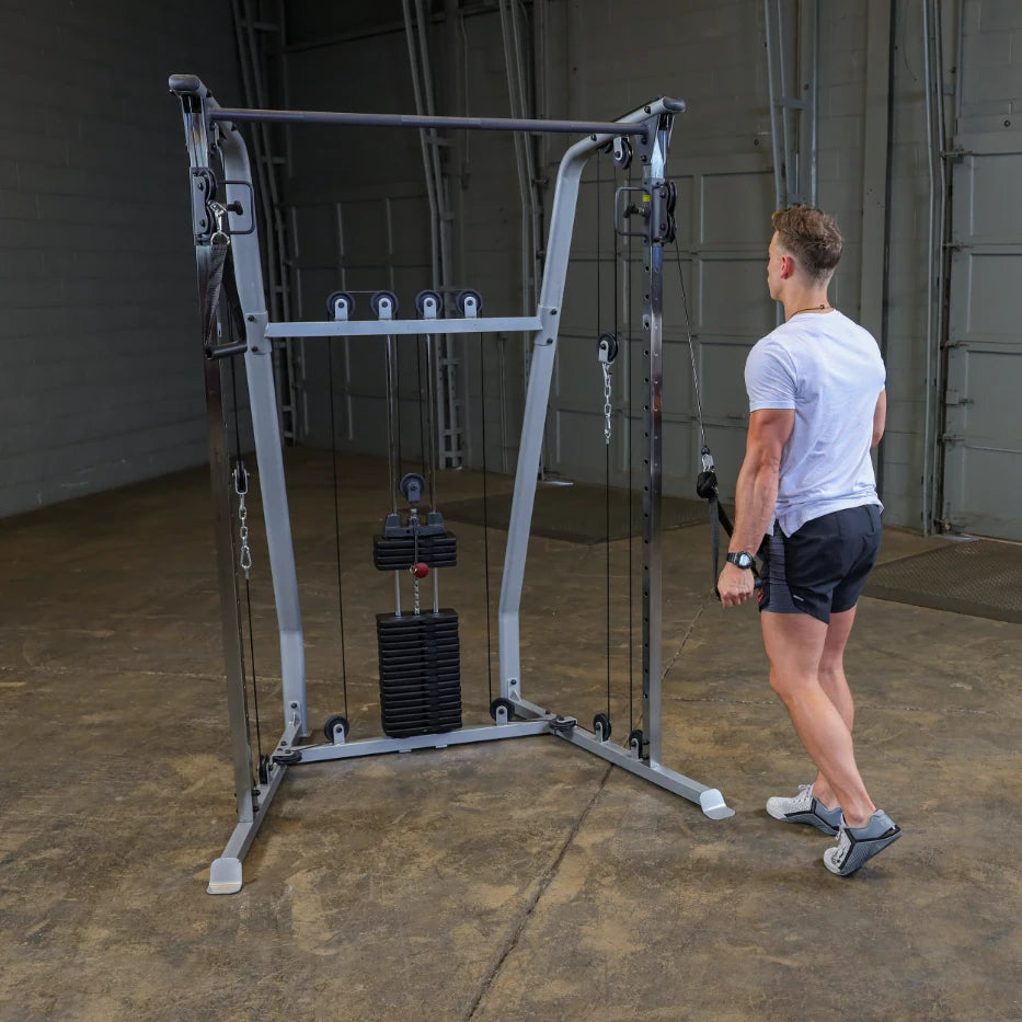 A person exercising with a cable machine in a gym setting, demonstrating strength training. The machine features adjustable weights and multiple pulley systems.